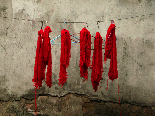 Red hand dyed yarn drying on the side of the street