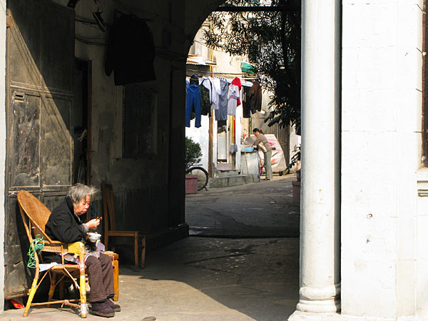 Elderly woman sitting in the sun. Young woman washing dishes.